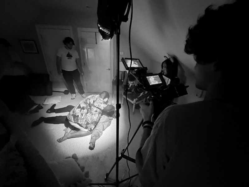 Behind the scenes — actors lit by a single spotlight while the crew films