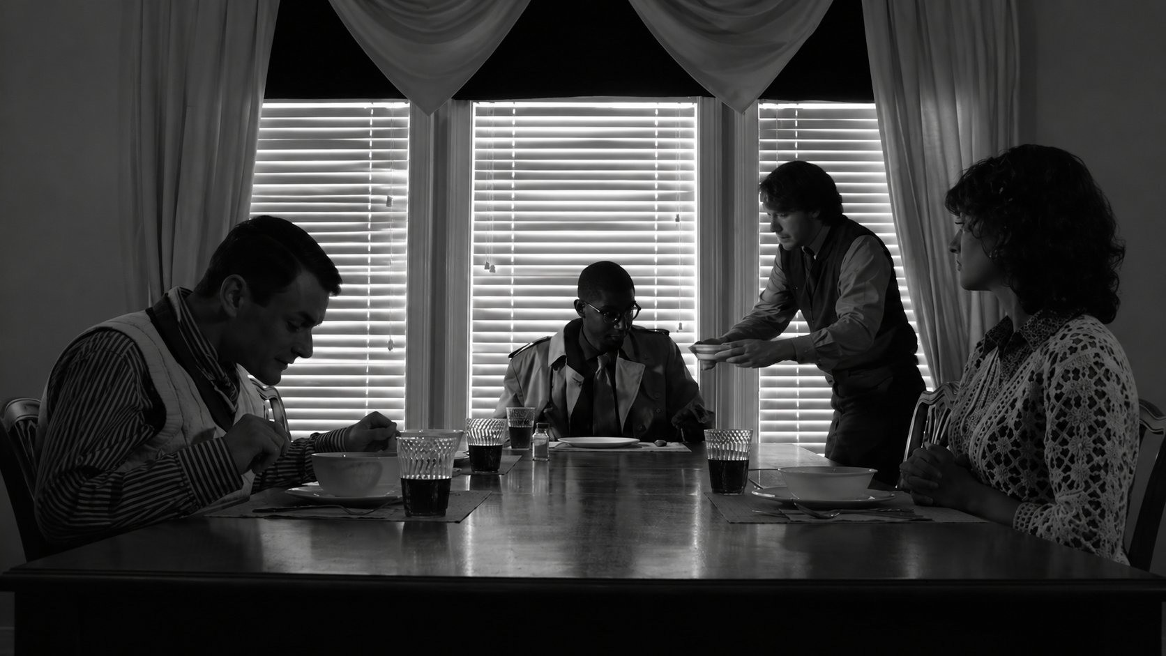 Production still from Pass The Salt — four characters at a backlit dinner table, black and white
