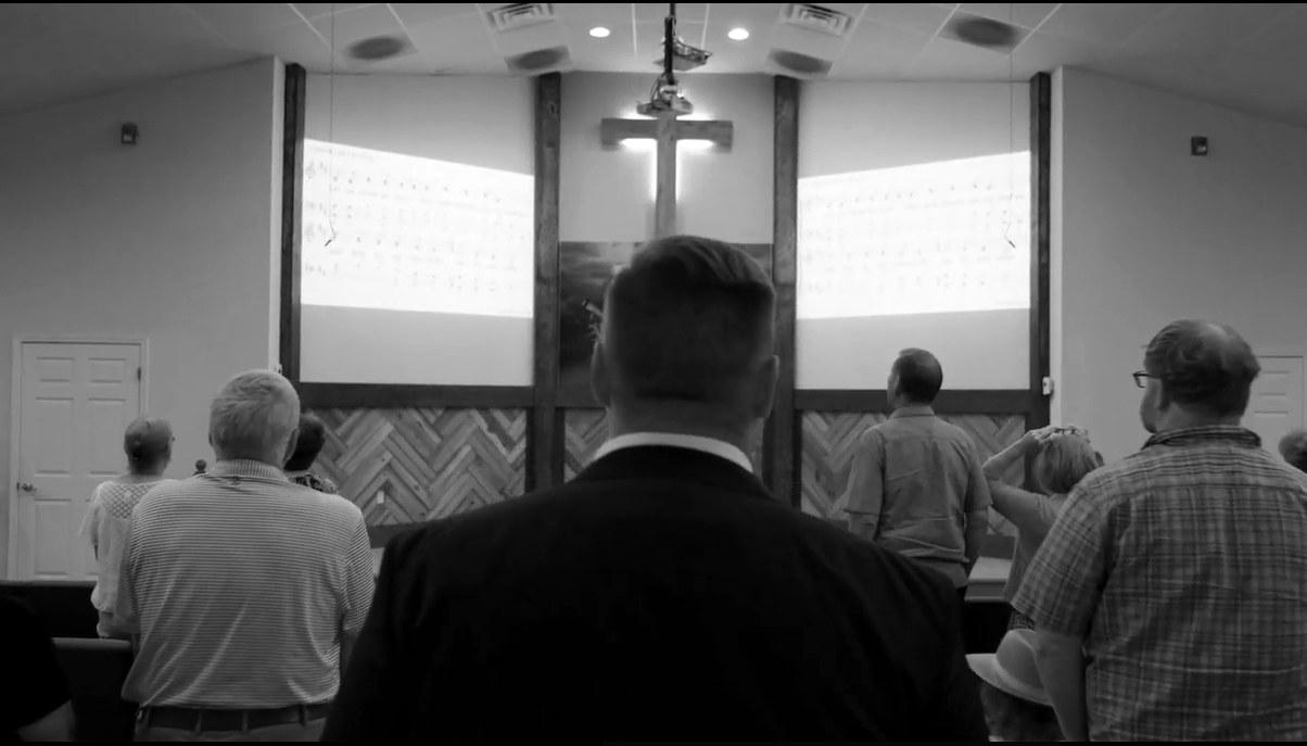 Still from the Upstate Church commercial — congregation during worship, black and white